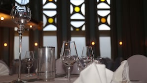 Una mesa de comedor con copas de vino y un vaso de agua, frente a un fondo de vidrieras.