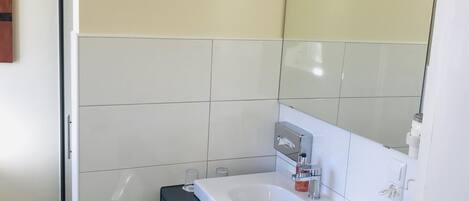 Un bany modern amb un lavabo blanc, un mirall i una zona de dutxa.