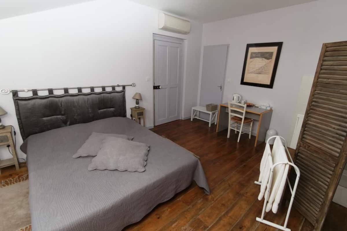 A bedroom with a bed, bedside table, lamp, desk, chair, and a drying rack.