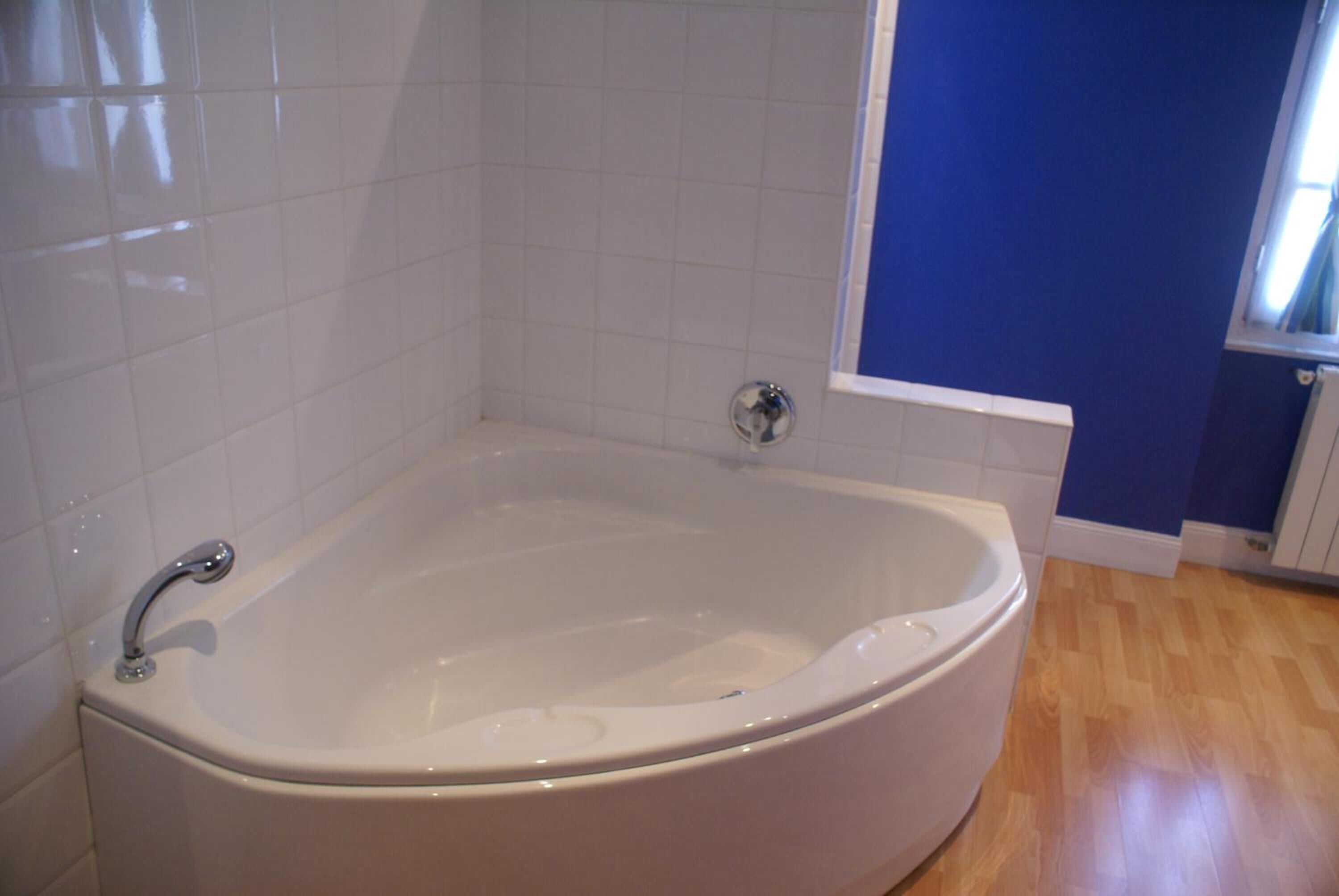 A bathroom with a white bathtub, white tiled walls, and wooden flooring.