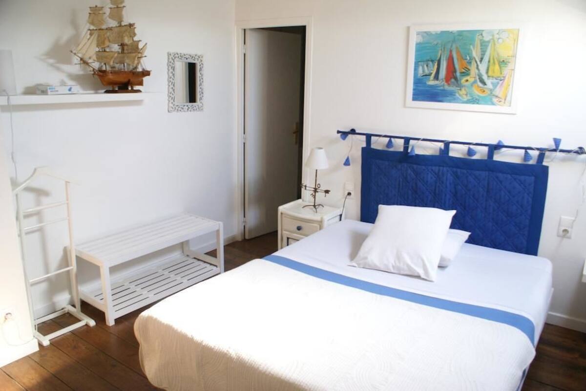 A bedroom with a bed, a nightstand, a lamp, a shelf with a ship model, and a painting.