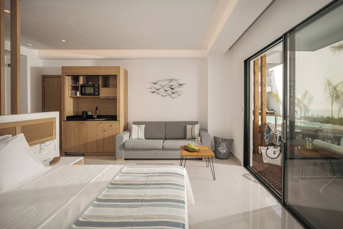 Ein modernes Hotelzimmer mit Bett, Sofa, Couchtisch, Küchenzeile und einem großen Fenster mit Blick.