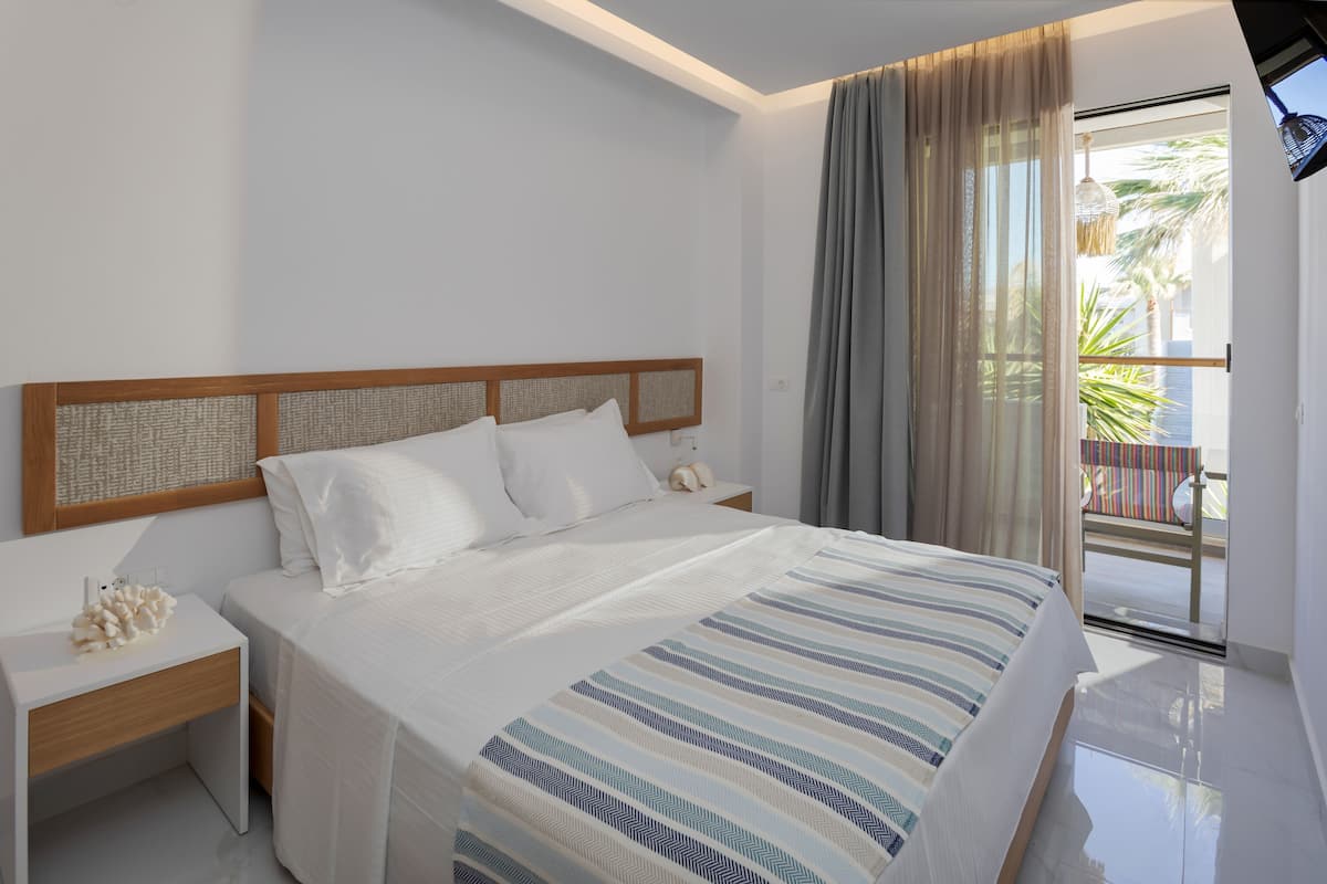 Ein modernes Hotelzimmer mit einem großen Bett, einem Holzkopfende, einem Nachttisch und Blick auf den Balkon.