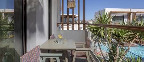 A balcony with a table and chairs, a hanging light fixture, and a view of a swimming pool.