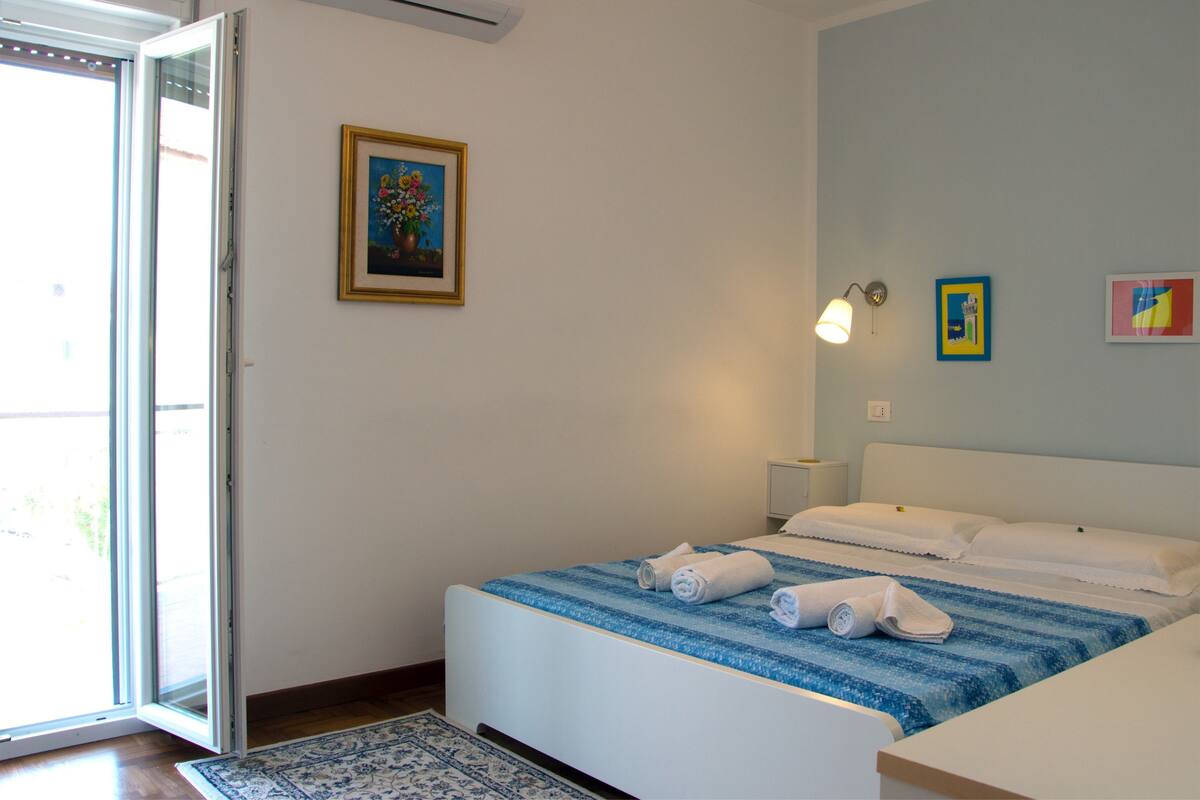 A bedroom with a bed, a nightstand, a wall-mounted lamp, and a door leading to a balcony.