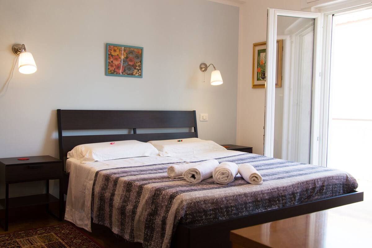 A neatly made bed with a striped blanket, two bedside lamps, and a small table with a red object on it.