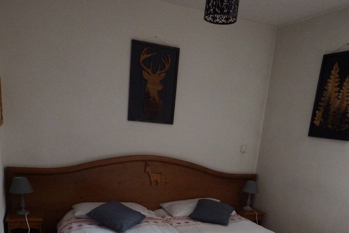 Un lit double avec une tête de lit en bois, deux tables de chevet avec des lampes et deux tableaux accrochés au mur.