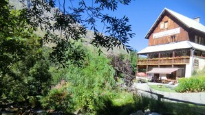 A rustic wooden building with a balcony, surrounded by lush greenery and a flowing stream. - Auberge Du Pont De L'Alp (Monetier-les-Bains)
