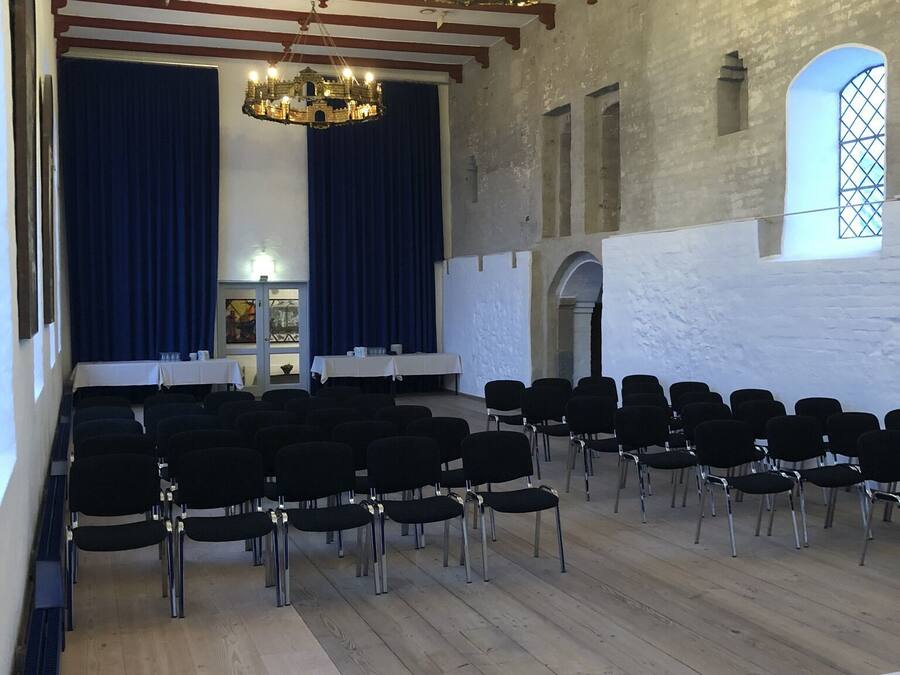 A church interior with pews, a chandelier, and a stage with curtains.