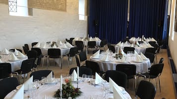 A banquet hall with round tables set for a formal event, featuring white tablecloths, silverware, and floral centerpieces.
