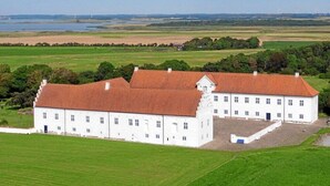 A large white building with a red roof, surrounded by green fields and a body of water in the background. - Danhostel Vitskøl Kloster (Logstor)