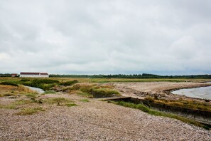 A gravelly landscape with a building in the distance, a water body, and a grassy area. - Danhostel Vitskøl Kloster (Logstor)