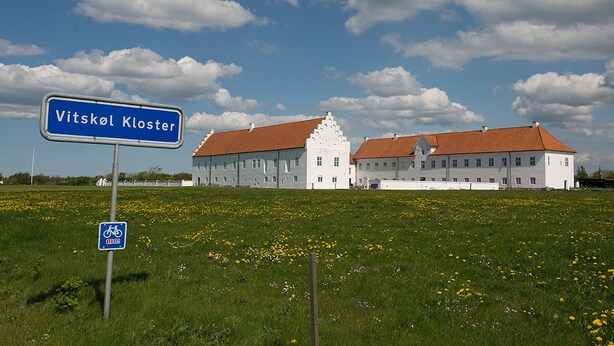 A large white building with a red roof, labeled "Vitskol Kloster," in a grassy field with yellow flowers. - Danhostel Vitskøl Kloster (Logstor)