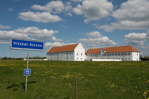 A large white building with a red roof, labeled "Vitskol Kloster," in a grassy field with yellow flowers. - Danhostel Vitskøl Kloster (Logstor)