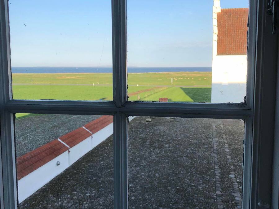 Una ventana con vista a un campo verde y un edificio con techo rojo.