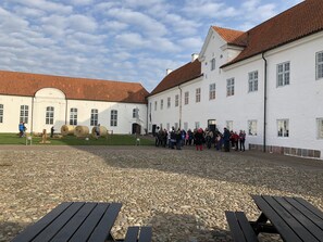 A courtyard with a cobblestone ground, white buildings with red-tiled roofs, and a group of people gathered in the center. - Danhostel Vitskøl Kloster (Logstor)
