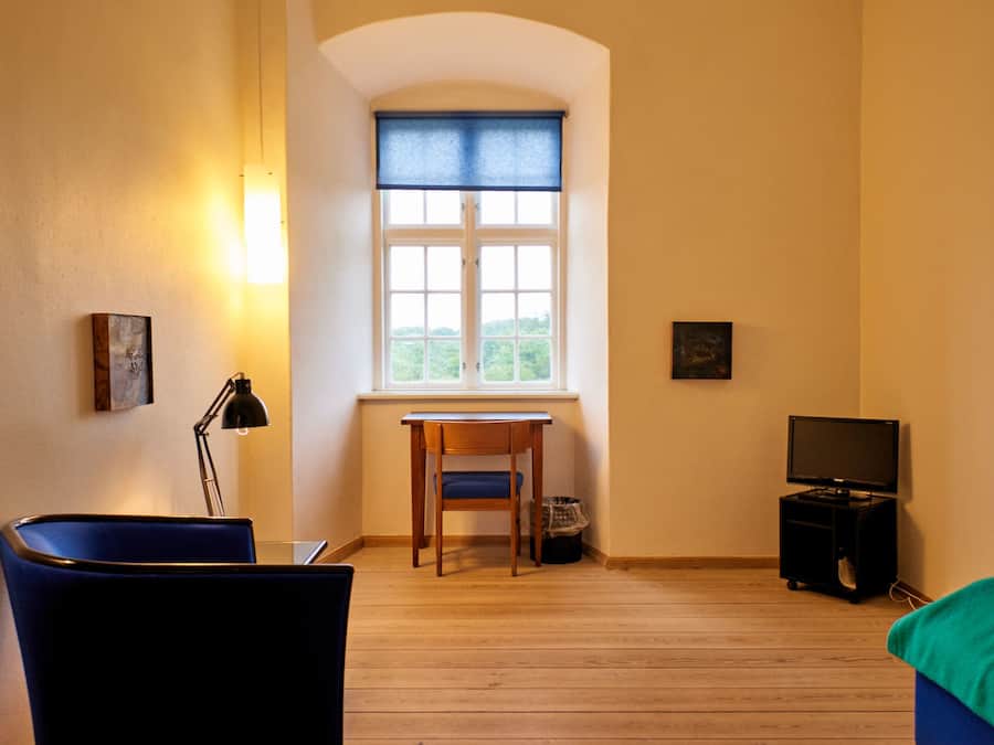 Ett rum med trägolv, ett skrivbord med en stol, ett fönster med utsikt, en tv och en lampa.