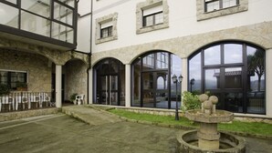 A building with stone arches and large windows, a fountain, and outdoor seating. - Hotel Balneario Baños da Brea (Vila de Cruces)