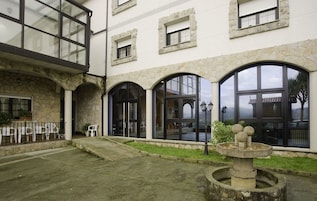 Un edificio con arcos de piedra y ventanas amplias, una fuente y asientos al aire libre.