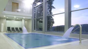Una piscina interior con paredes de vidrio transparente, diseño moderno y vistas al exterior.