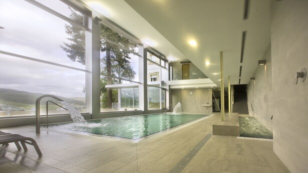 A modern indoor swimming pool with a view of the outdoors, large windows, and a minimalist design. - Hotel Balneario Baños da Brea (Vila de Cruces)