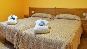 A hotel room with two beds, a chair, a desk with a television, and towels on the beds. - Hotel Balneario Baños da Brea (Vila de Cruces)