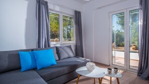 Una sala de estar moderna con un sofá gris, cojines azules, una mesa de centro blanca y vistas a través de amplios ventanales corredizos.