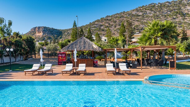 Una piscina con sillas de descanso y zona sombreada, rodeada de follaje y un telón de fondo montañoso.