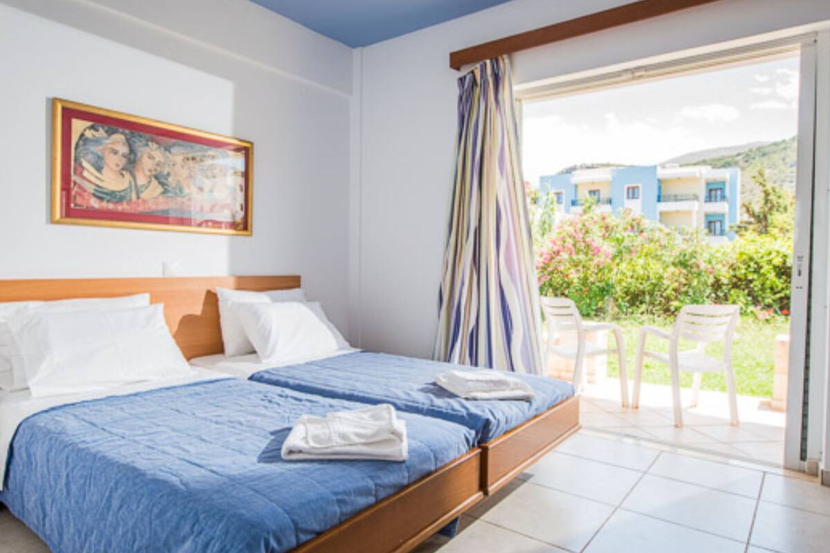 A hotel room with a bed, a painting, and a balcony with chairs.