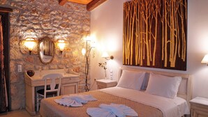 Habitación de hotel con pared de piedra, cama con ropa de cama blanca, escritorio con silla y espejo fijado a la pared.