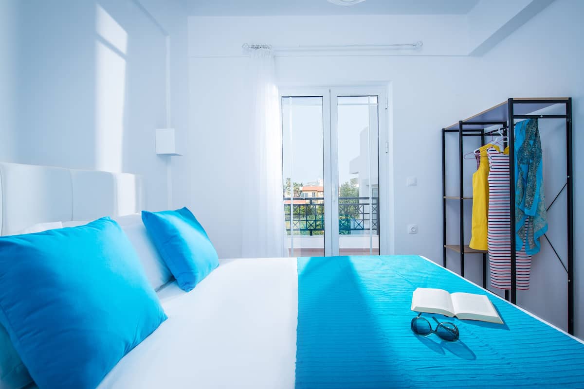 A modern hotel room with a bed, a balcony, and a clothing rack.