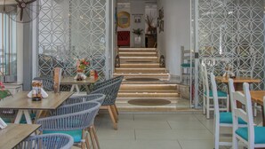 Interior de un restaurante con sillas de mimbre, una recepción y una escalera que sube a la planta superior.