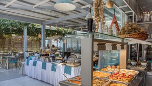 Zona de bufé con diversas opciones de comida, un área de estar con mesas y sillas, y un techo decorativo con luces colgantes.