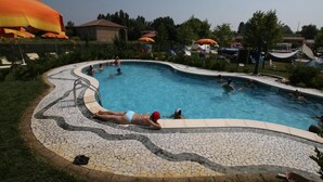 A swimming pool with tiled edges and a mosaic pattern, surrounded by lounge chairs and umbrellas.