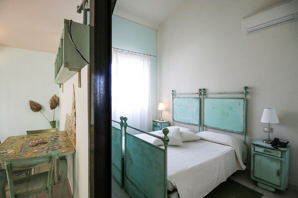 A room with a bed, a bedside table with a lamp, a small table with a chair, and a decorative wall piece. - Lucciole nella nebbia (Bondeno)
