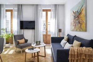 Ein modernes Wohnzimmer mit einem grauen Sessel, einem blauen Sofa, einem runden Couchtisch und einem an der Wand befestigten Flachbildfernseher.