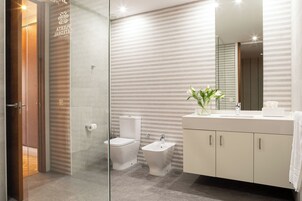 A modern bathroom with a glass shower enclosure, a toilet, bidet, and a vanity with a mirror.