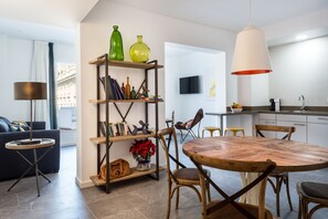 A modern living room with a round wooden dining table, a bookshelf with various decorative items, and a large pendant light. - Puerta Catedral Indias Lofts (Seville)