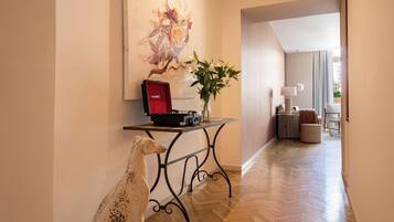 A hallway with a wooden floor, a table with a record player, a vase with flowers, and a painting on the wall.