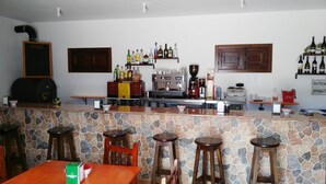 Angolo bar con un bancone in pietra, sgabelli, una macchina da caffè e scaffali con bottiglie.