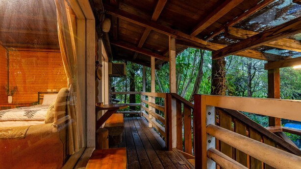 A wooden cabin with a covered porch, a bed, and a view of the forest. - Water Villa (Wujie)