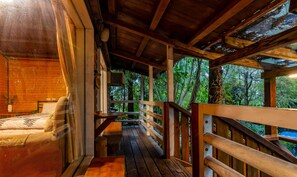 A wooden cabin with a covered porch, a bed, and a view of the forest. - Water Villa (Wujie)