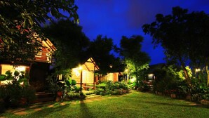 A well-lit garden area with a wooden cabin structure, surrounded by lush greenery and potted plants. - Water Villa (Wujie)