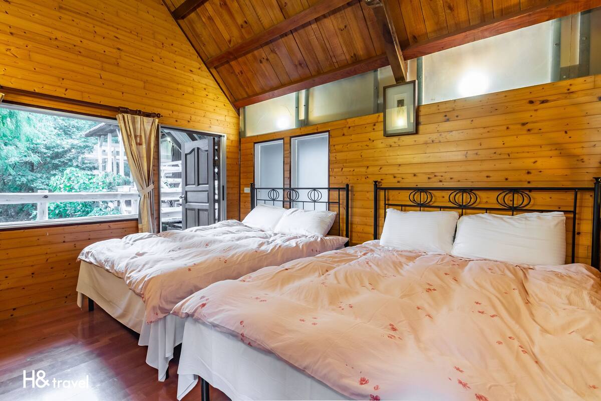 Ein Zimmer in einer Holzhütte mit zwei Betten, einem großen Fenster und Blick auf Grünland.