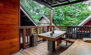 Une terrasse en bois avec une table et des bancs, entourée d’une balustrade en bois et offrant une vue sur la verdure.