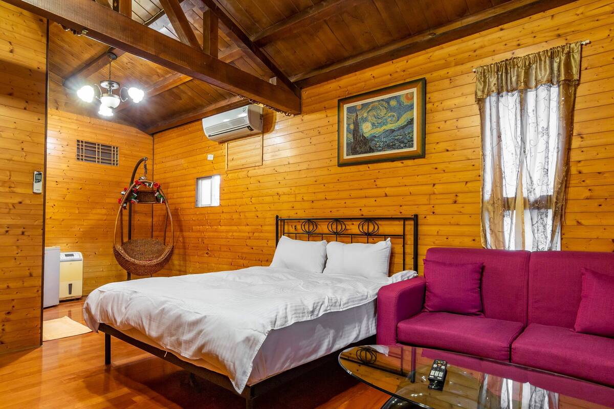 Ein Zimmer in einer Holzhütte mit einem Bett, einem pinken Sofa, einem Hängesessel und einem Bild an der Wand.