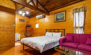 Une pièce de style cabane en bois, avec un lit, un canapé rose, un fauteuil suspendu et un tableau au mur.