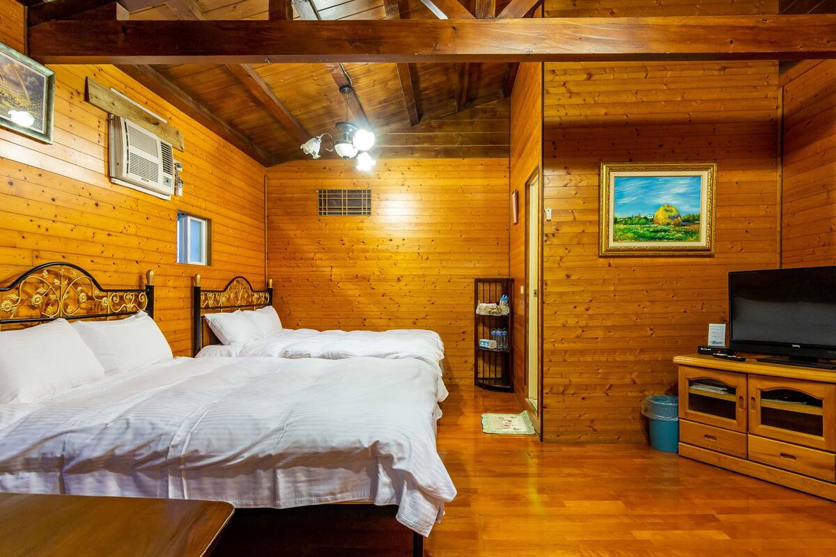 Ein Holzhütten-Zimmer mit zwei Betten, einem Fernseher und einem kleinen Schrank.