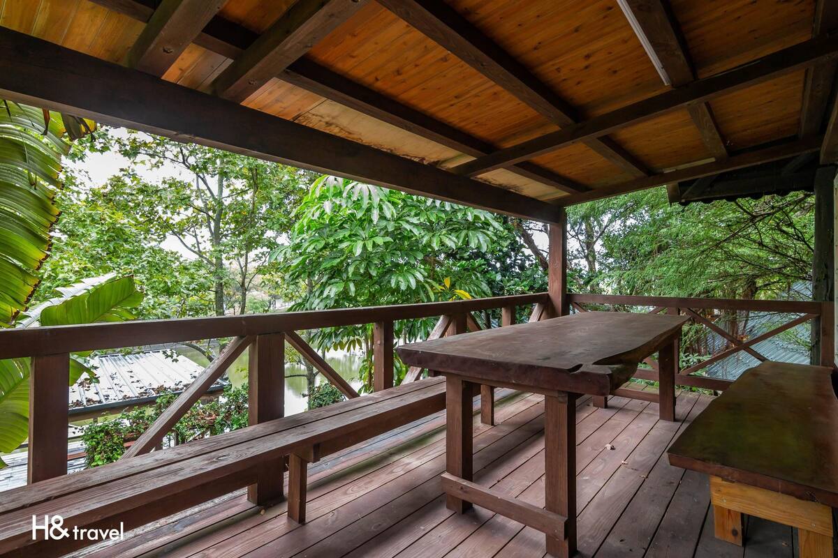 Eine Holzterrasse mit Tisch und Bänken, mit Blick auf ein Gewässer und üppiges Grün.