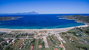 An aerial view of a coastal area with a large body of water, a mountain in the background, and a mix of residential and agricultural buildings.